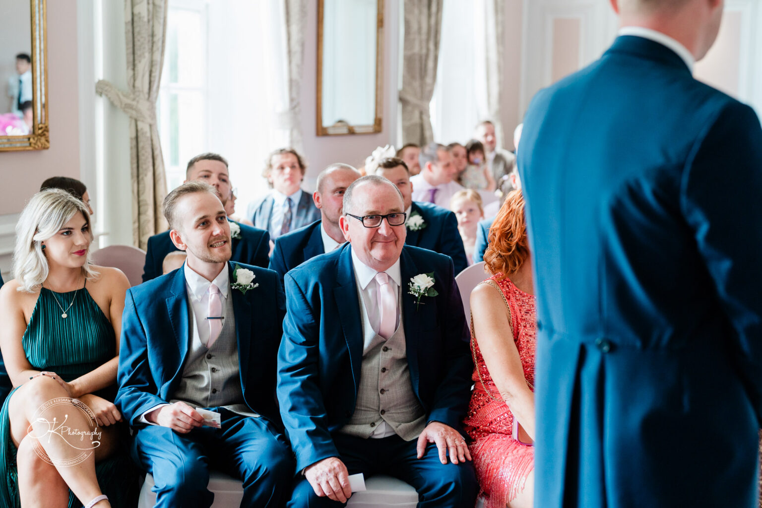 A group of people seated in a hotel event room, dressed in formal attire, attending a ceremony.