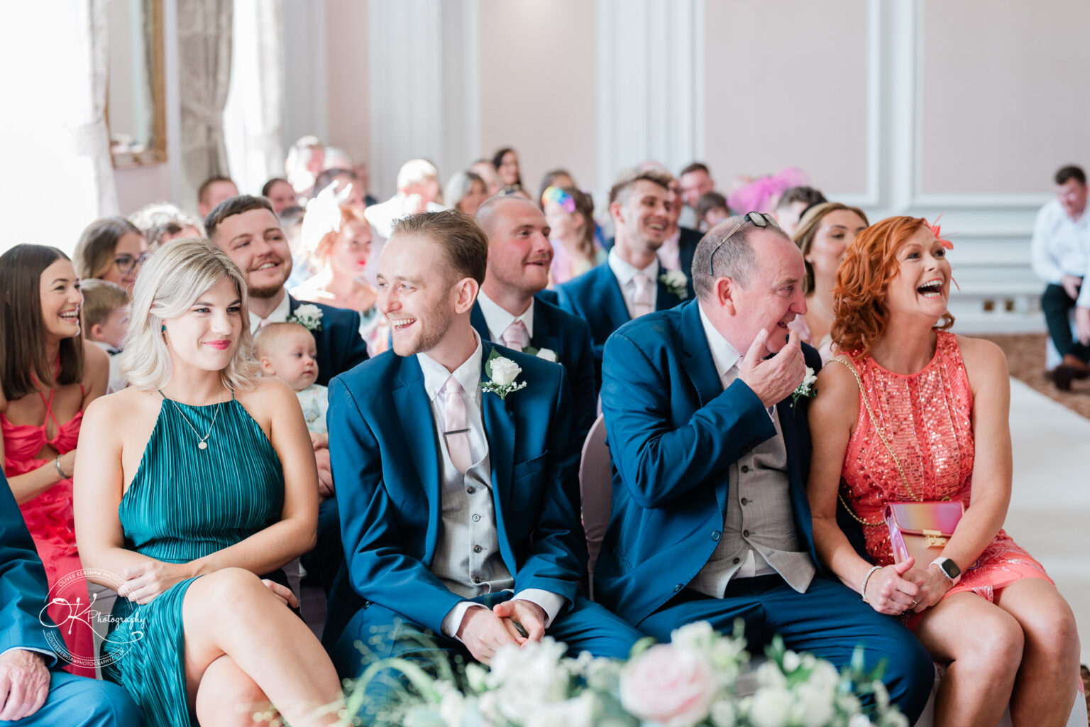 Guests seated at a wedding ceremony, smiling and laughing, at Bosworth Hall Hotel.