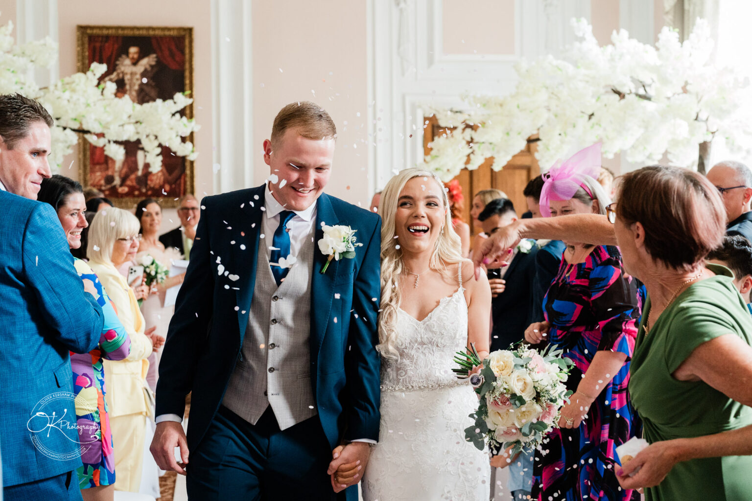 A newlywed couple walks down the aisle as guests throw confetti in celebration at Bosworth Hall Hotel.