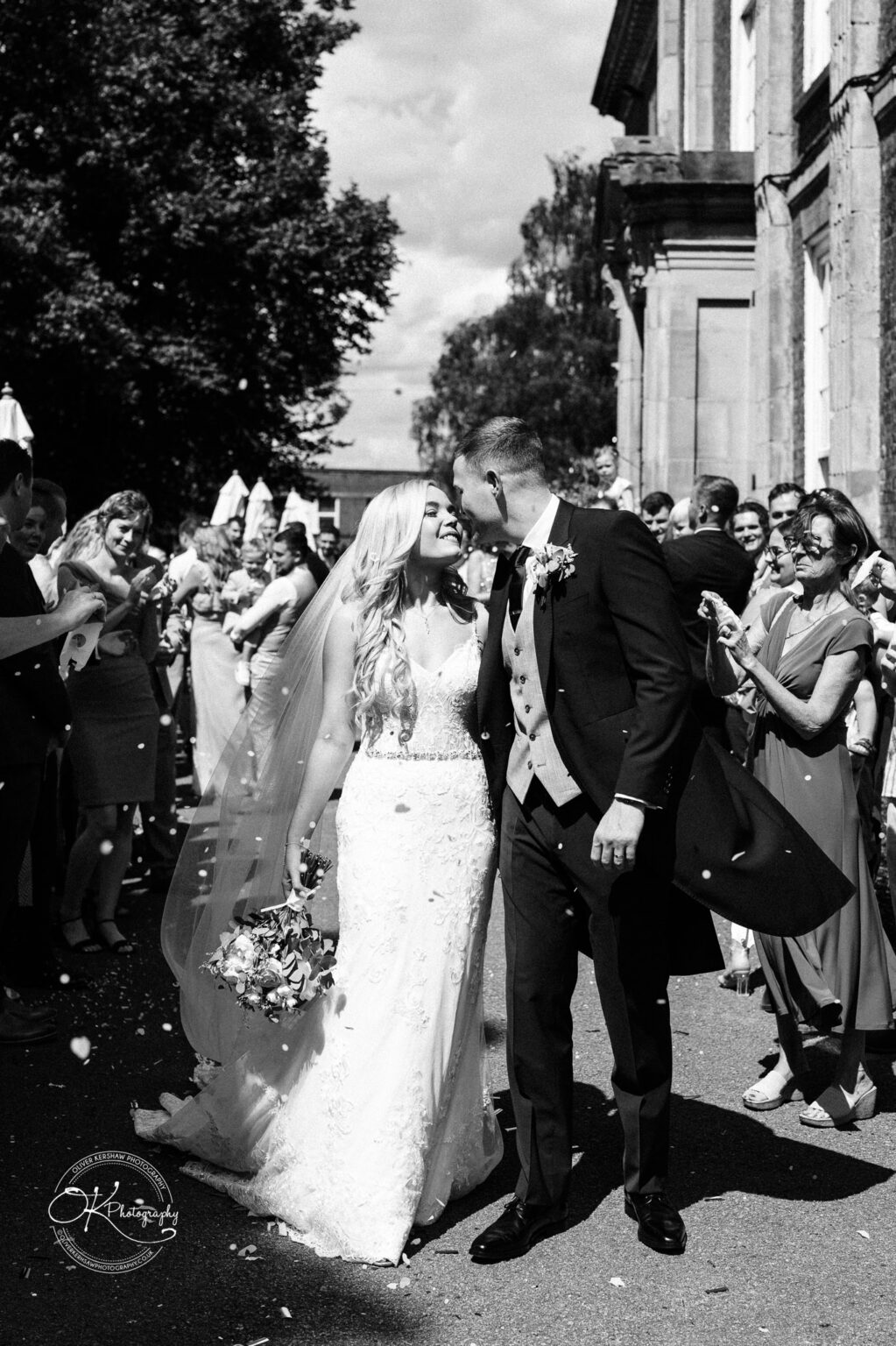 Bride and groom kissing outside Bosworth Hall Hotel surrounded by guests.