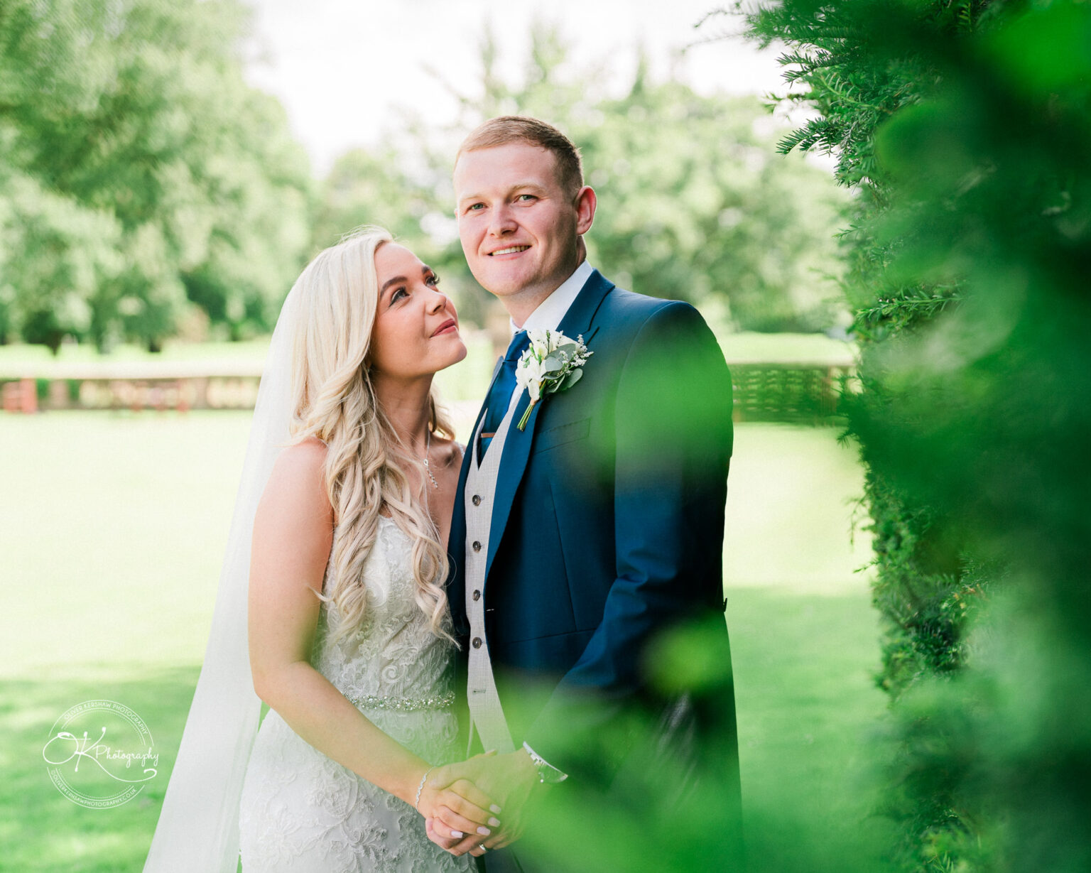 A bride and groom posing outdoors, with greenery and trees in the background at Bosworth Hall Hotel.