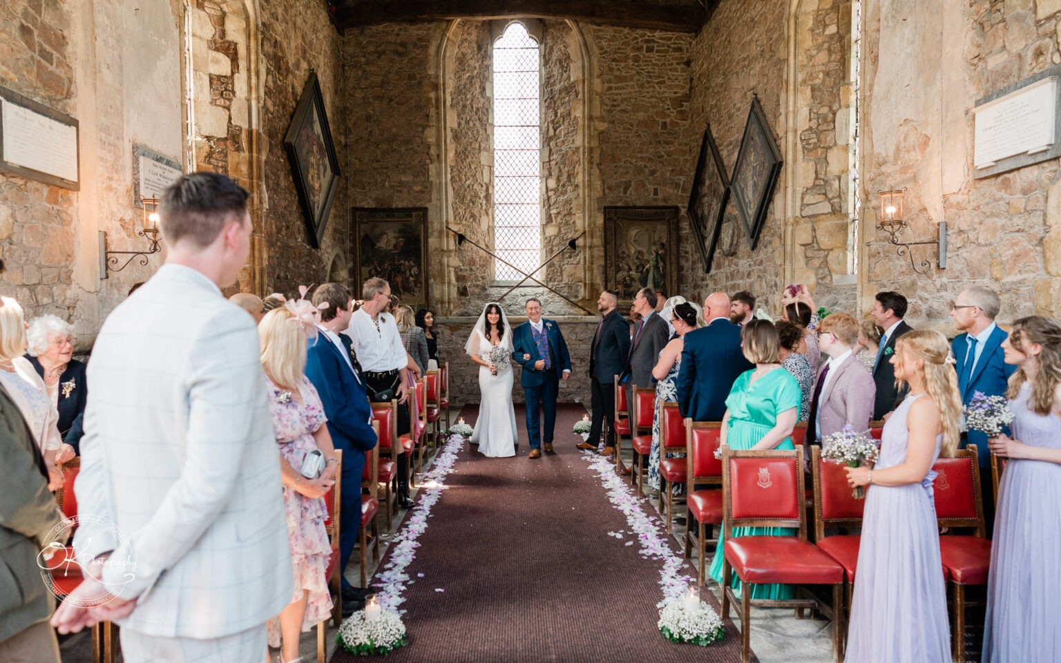 Rothley Court Hotel wedding photography Bride walking down the aisle with her father in a stone-walled church, surrounded by seated guests.