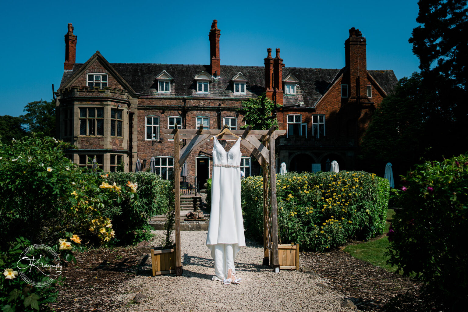 Rothley Court Hotel wedding photography Wedding dress hanging on a wooden archway in a garden with an old mansion in the background.