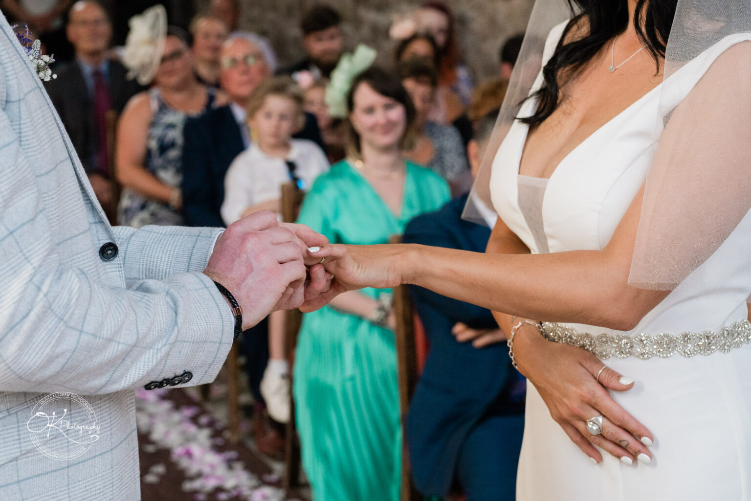 Rothley Court Hotel wedding photography A bride and groom exchange rings during a wedding ceremony, with guests seated and watching in the background.
