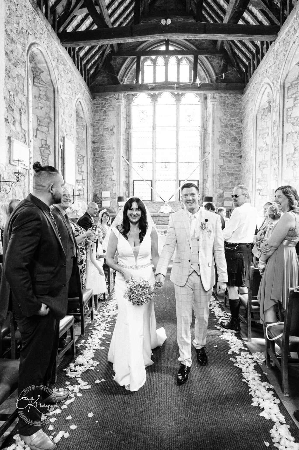 Rothley Court Hotel wedding photography Bride and groom walking down the aisle in a stone chapel, surrounded by smiling guests.