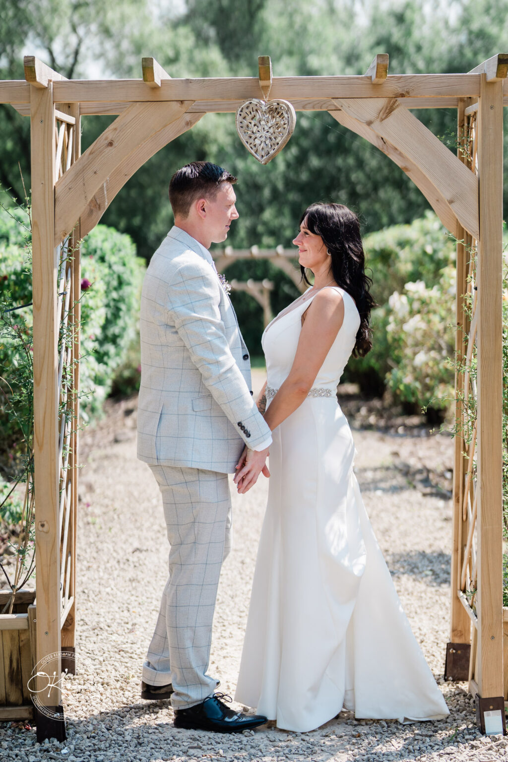 Rothley Court Hotel wedding photography Couple standing under a wooden archway, facing each other and holding hands, with greenery in the background.