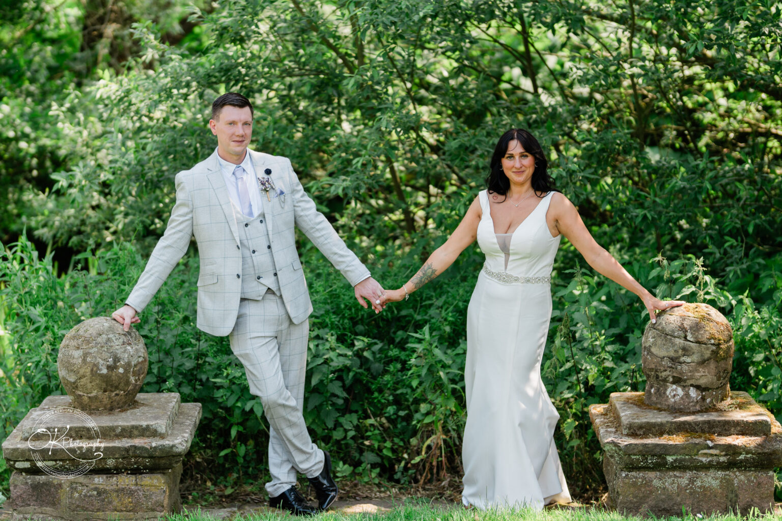 Rothley Court Hotel wedding photography Bride and groom holding hands while standing beside stone posts in a lush garden.