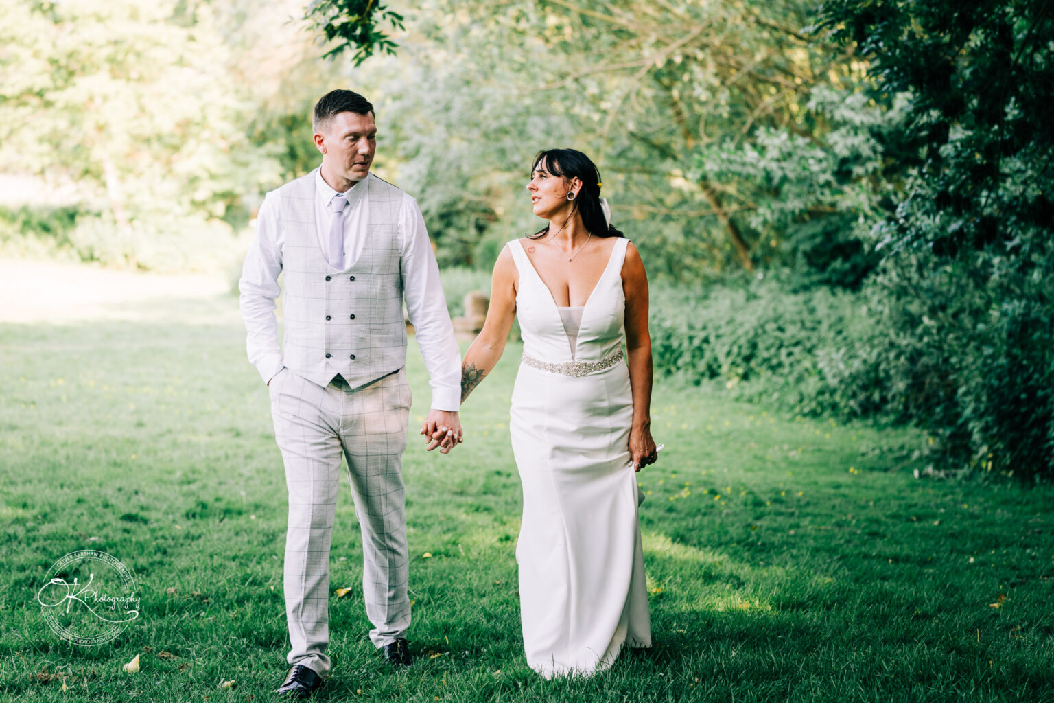 Rothley Court Hotel wedding photography Bride and groom holding hands while walking on a grassy area, both looking at each other lovingly.