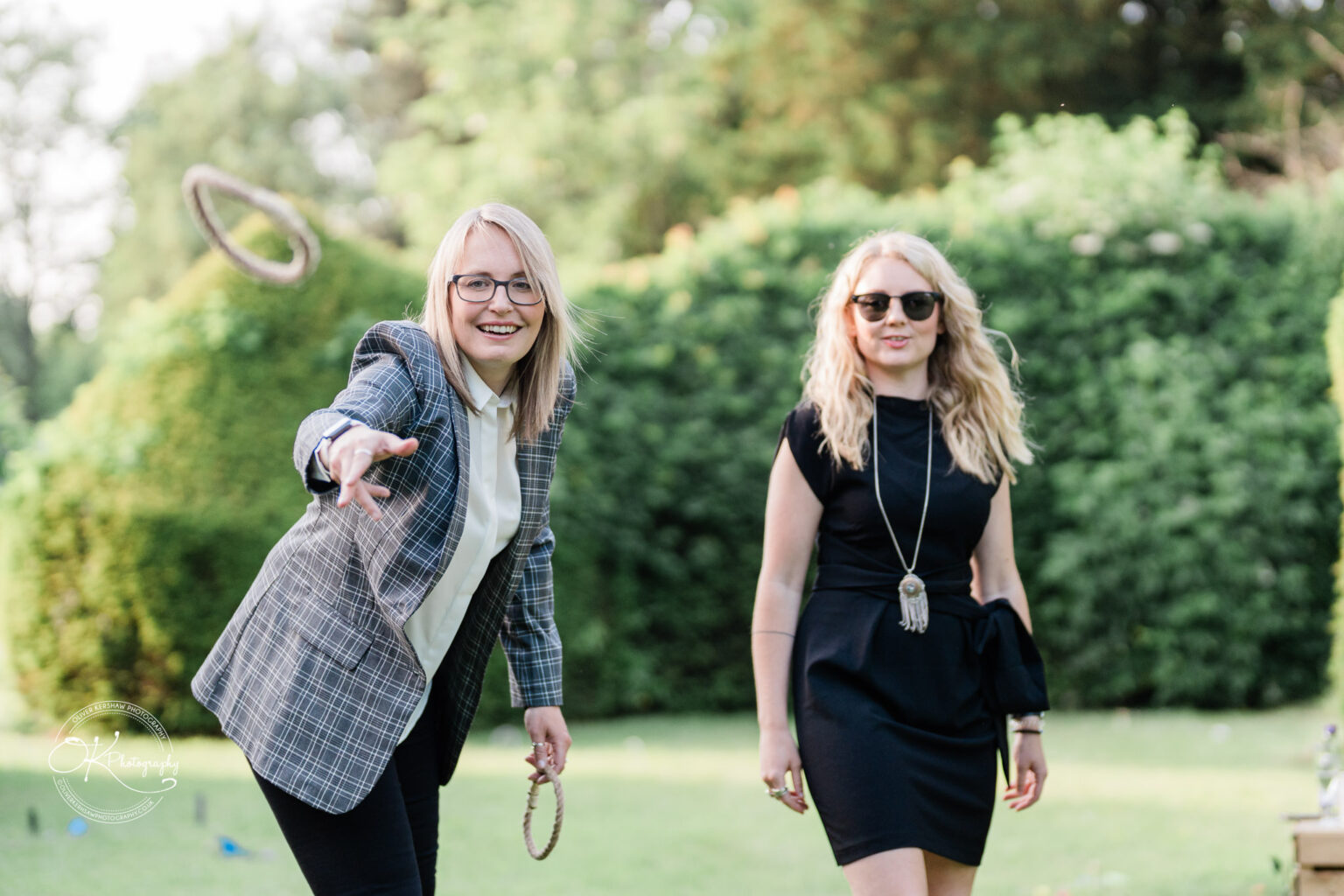 Rothley Court Hotel wedding photography Two women playing ring toss in a garden, one wearing a plaid blazer and glasses throwing, and the other in a black dress and sunglasses observing.