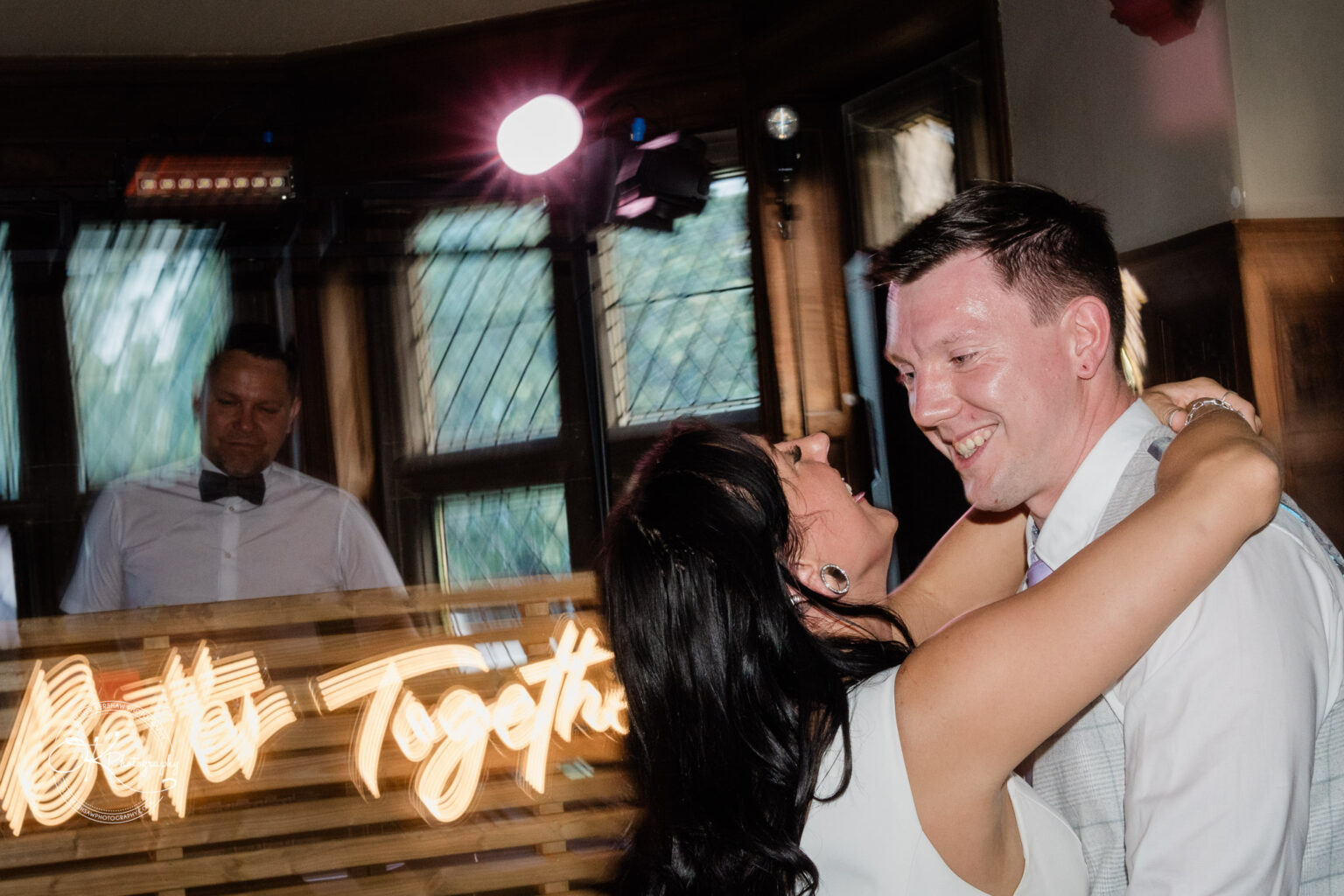 Rothley Court Hotel wedding photography A couple dancing and smiling, with a DJ in the background and a neon sign reading "Better Together".