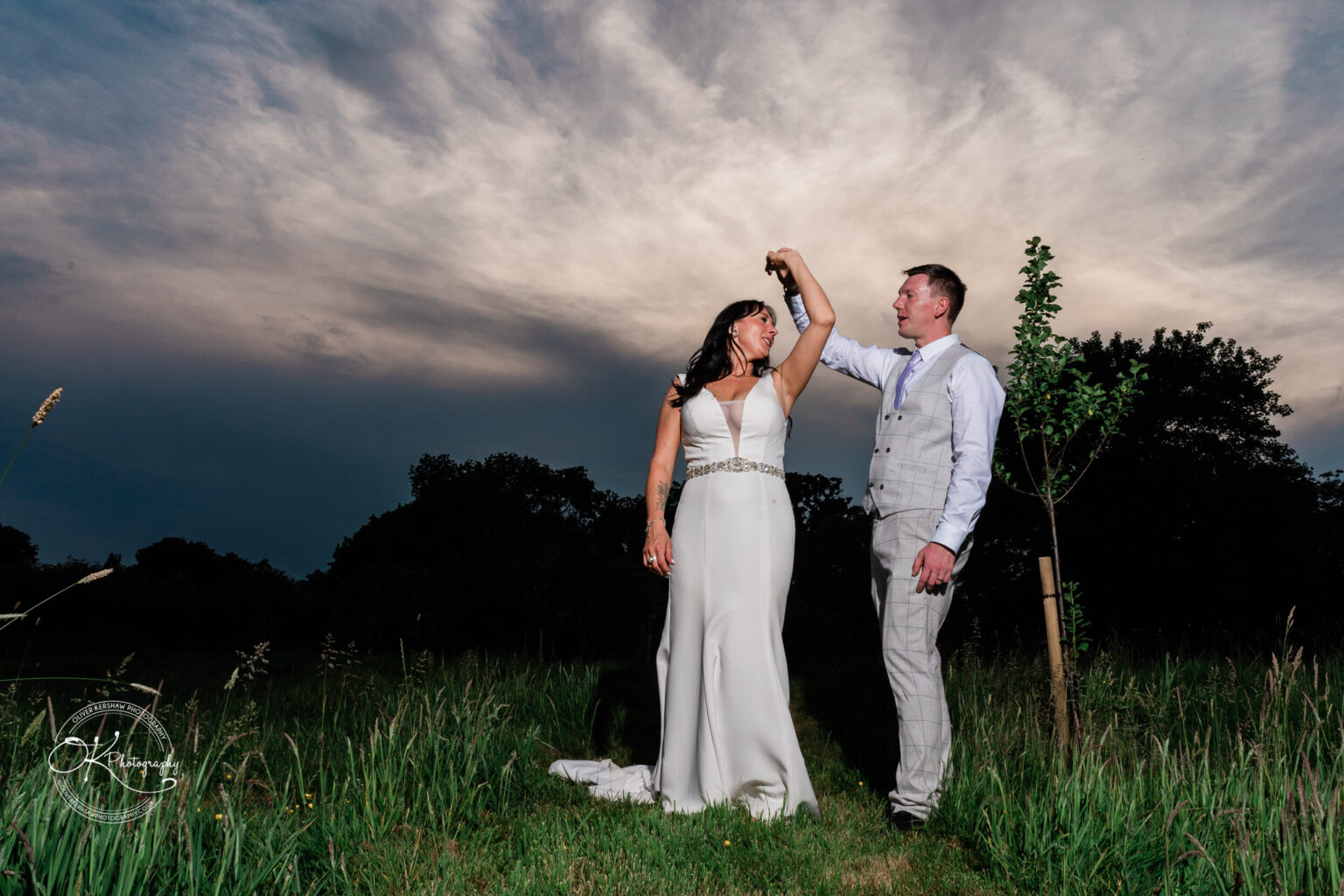 Rothley Court Hotel wedding photography A bride and groom stand in a grassy field at dusk, with the groom twirling the bride under his raised arm.