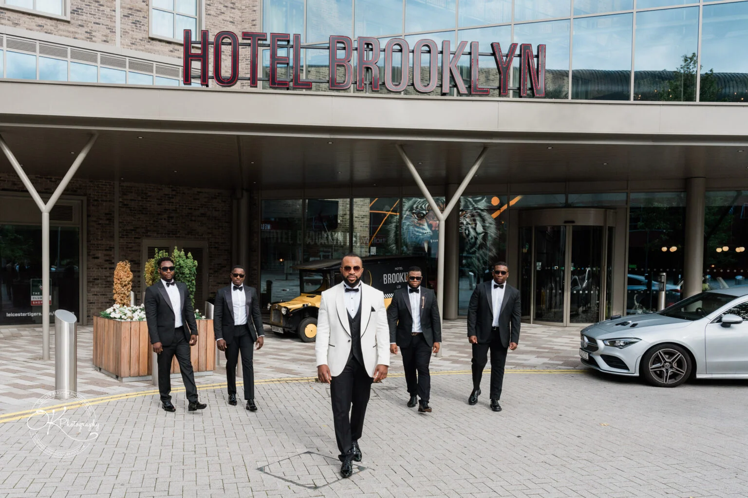 Five men in formal attire standing in front of Hotel Brooklyn.