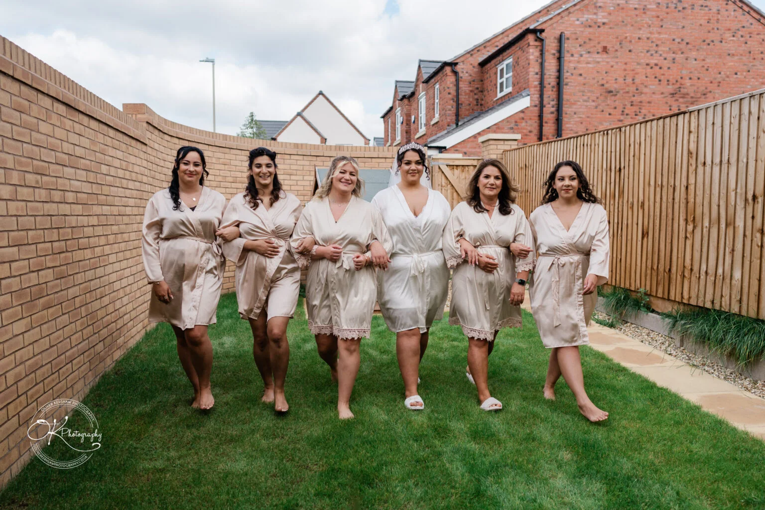 A bridal party in matching robes walking on a grass path outside.