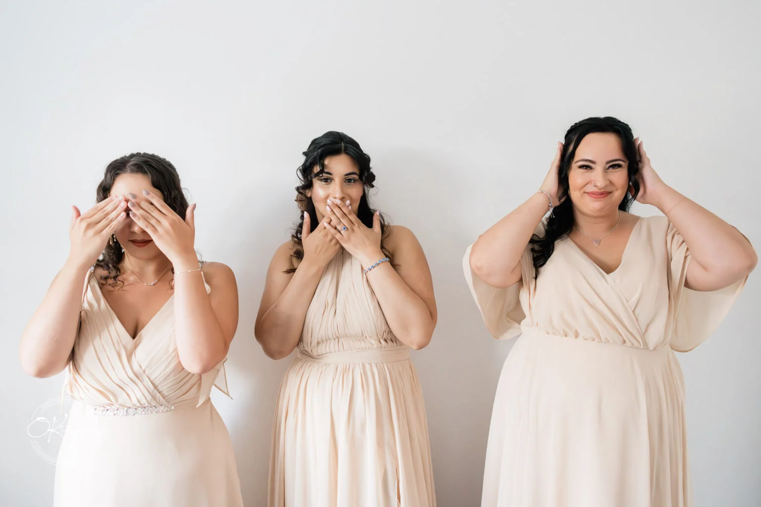 Three women in beige dresses pose facing the camera, mimicking the "see no evil, speak no evil, hear no evil" gesture.
