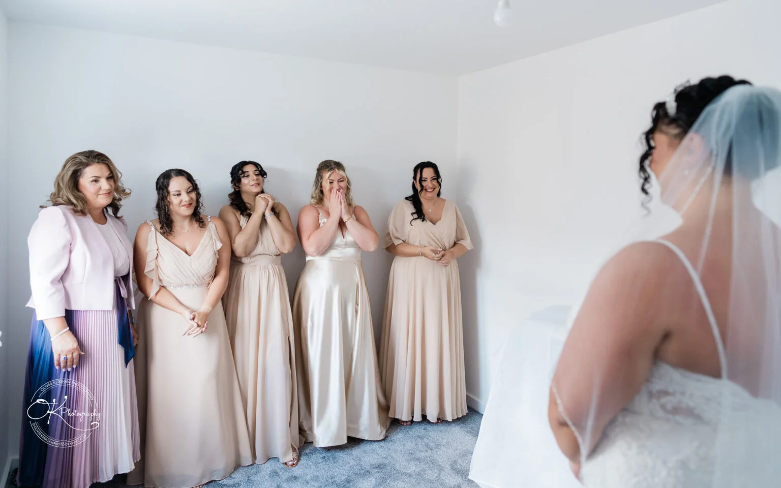 Five bridesmaids react emotionally while looking at the bride in her dress.
