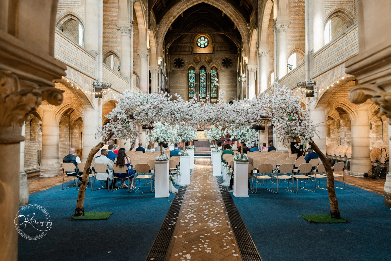 Interior of a church set up for a wedding, with rows of chairs and two large artificial cherry blossom trees lining the aisle.