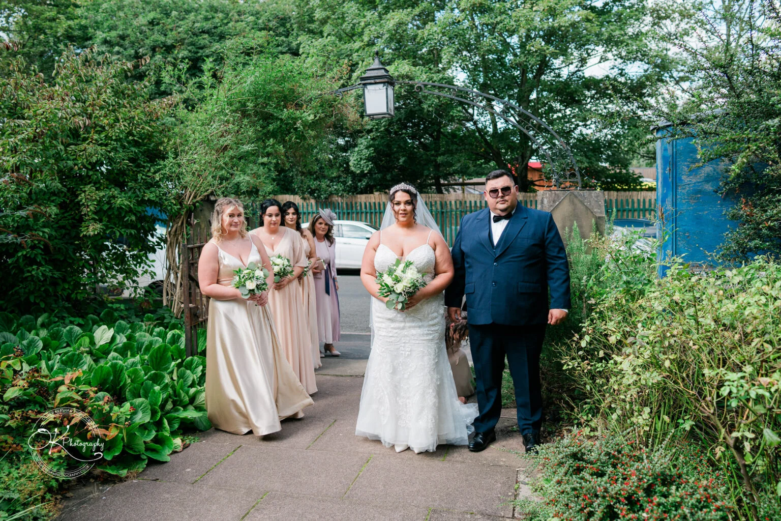 Bride and bridesmaids in pastel dresses, accompanied by a man in a dark suit, preparing for a wedding.