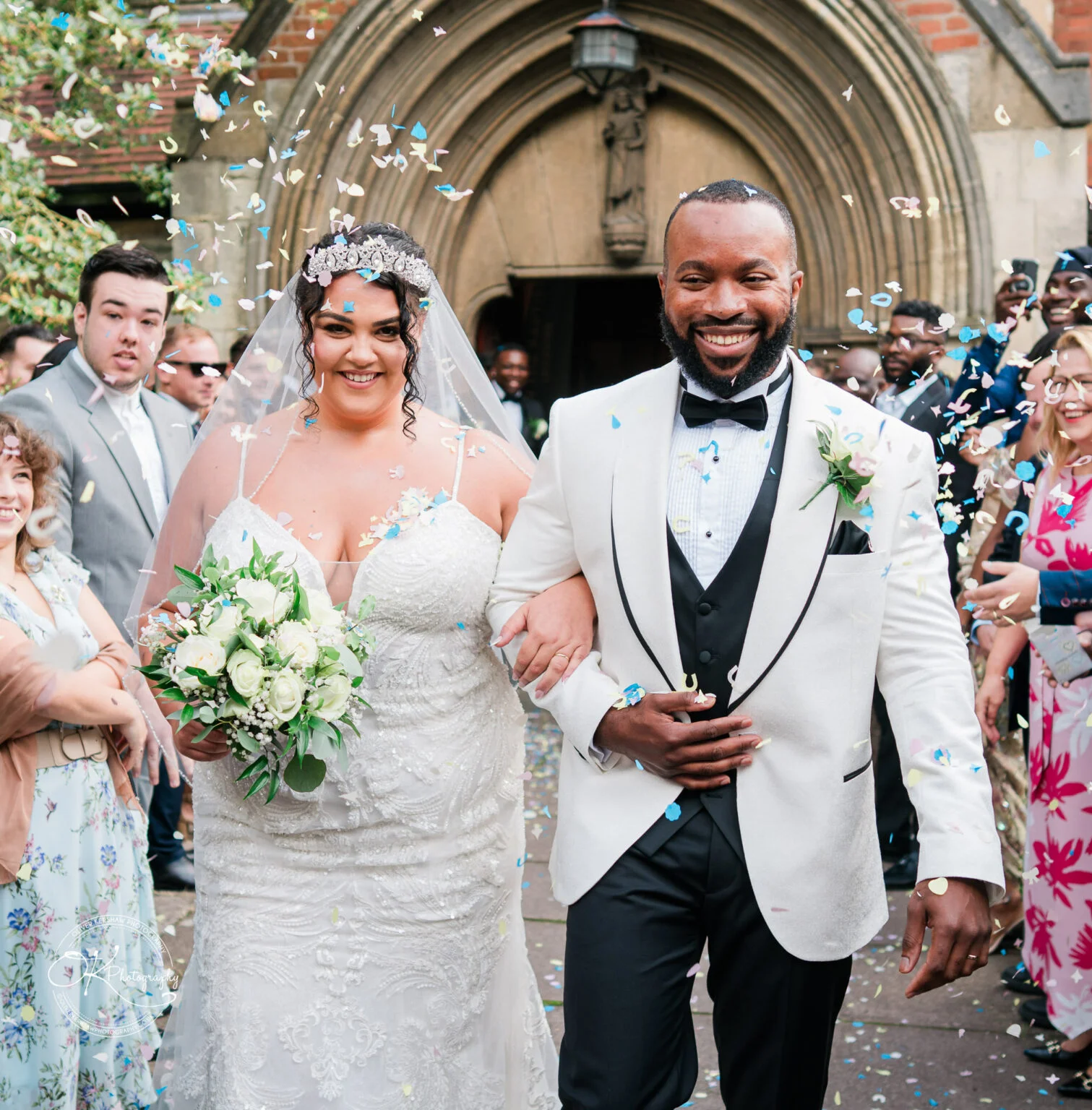 Bride and groom walking arm in arm through a crowd while being showered with confetti.