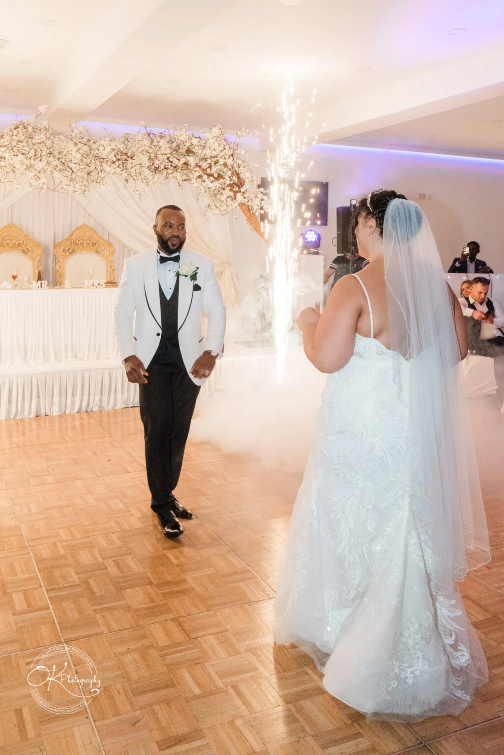 Bride and groom dance at their wedding reception with sparkling fireworks in the background.