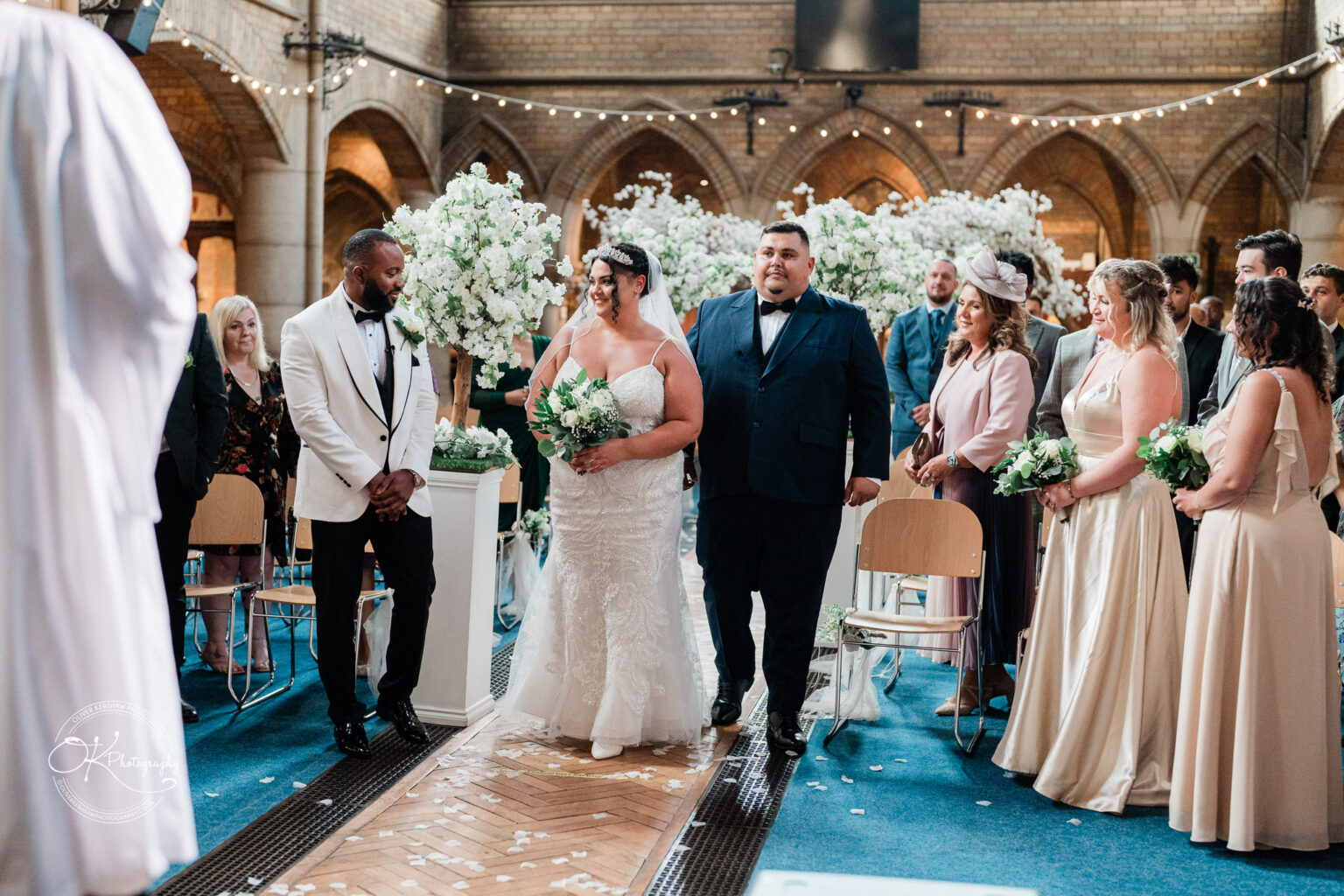 Symphony Rooms Wedding Photography Bride walking down the aisle with her father, surrounded by guests in an ornately decorated church.