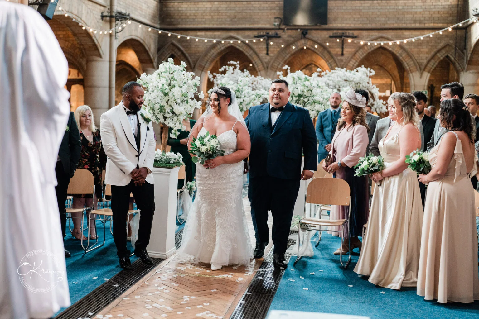 Bride walking down the aisle with her father, surrounded by guests in an ornately decorated church.
