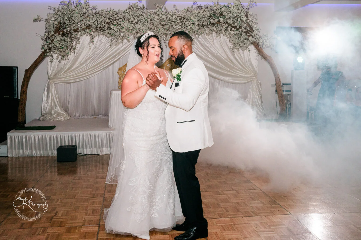 Bride and groom dancing at their wedding reception with mist and decorative backdrop in the background.