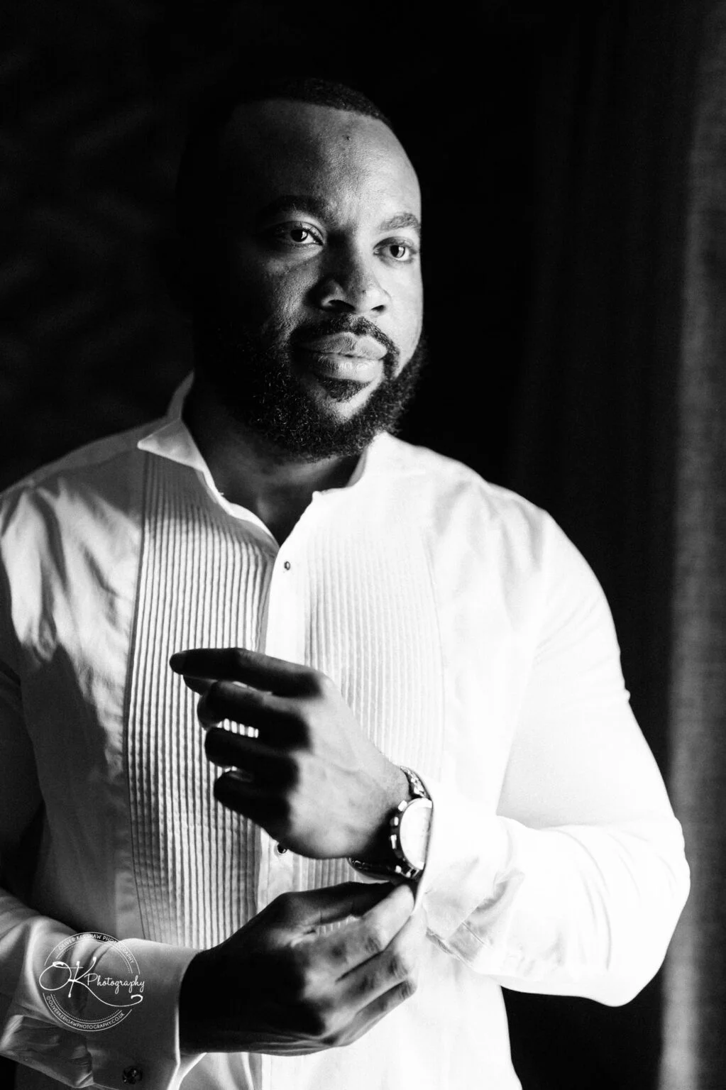 Black and white portrait of a man adjusting his watch, wearing a white dress shirt.