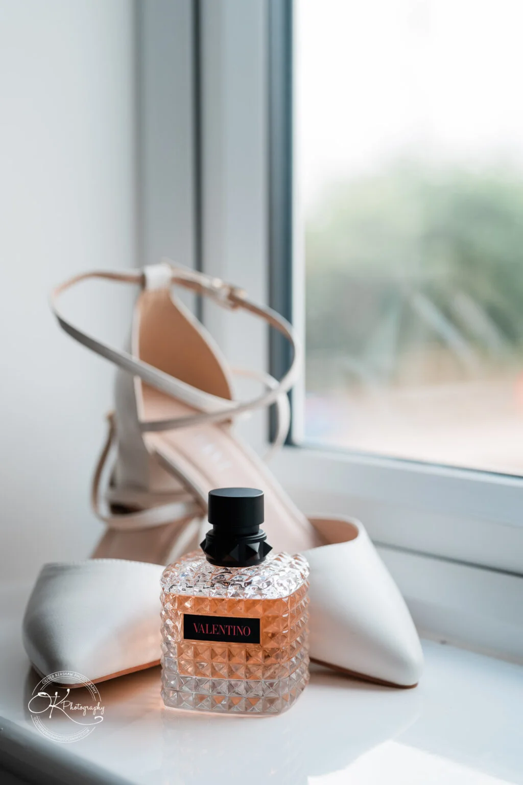 White high-heeled shoes and a Valentino perfume bottle on a windowsill.