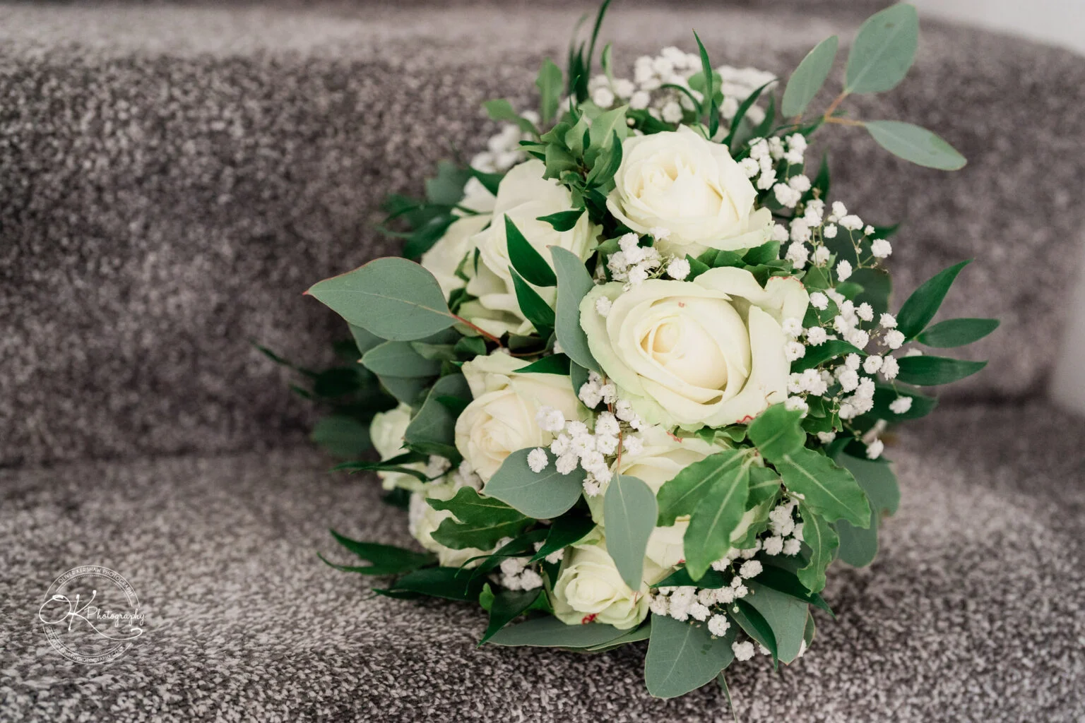 A bouquet of white roses with baby's breath and greenery placed on grey carpeted stairs.