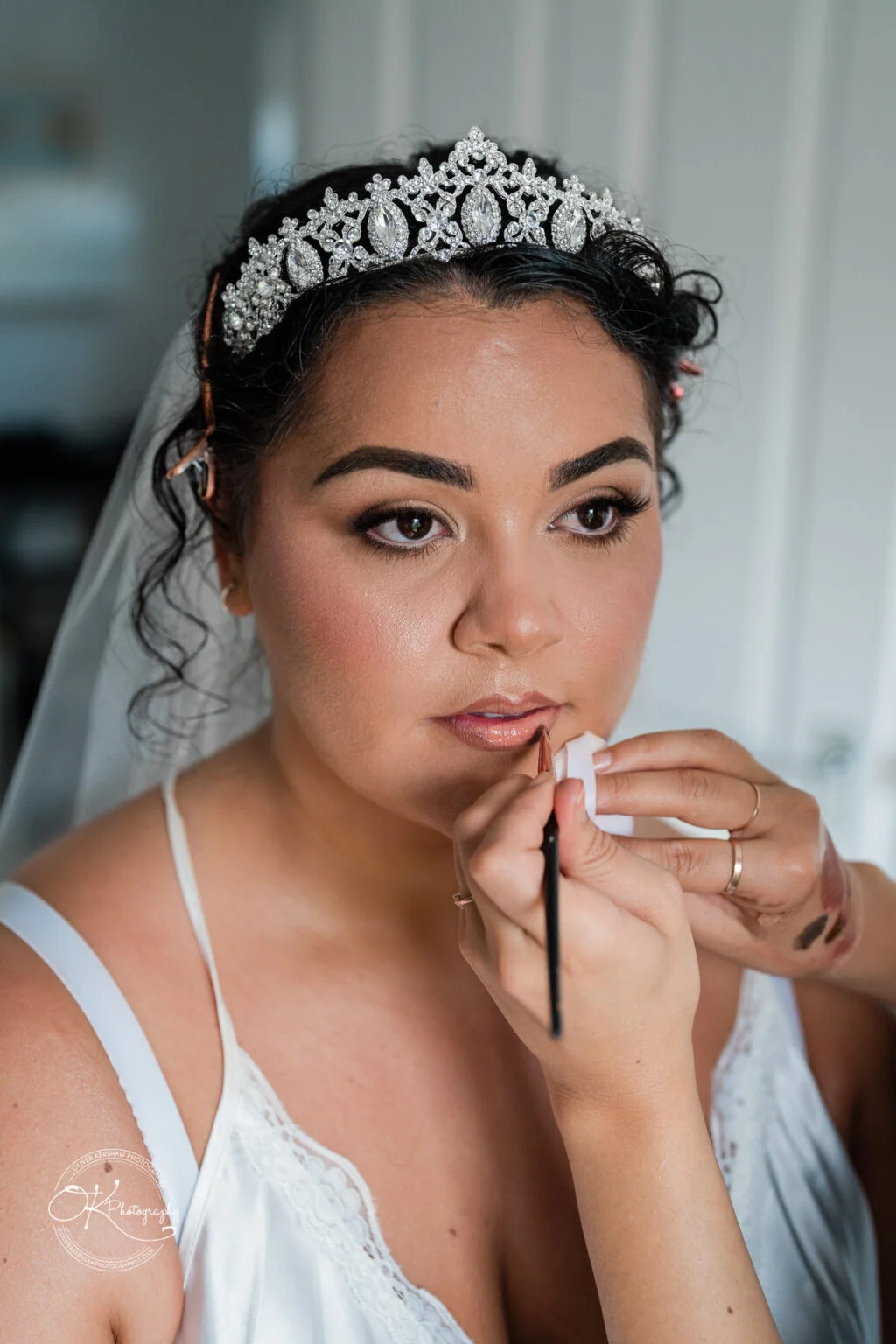 Bride wearing a jeweled tiara having her makeup done.