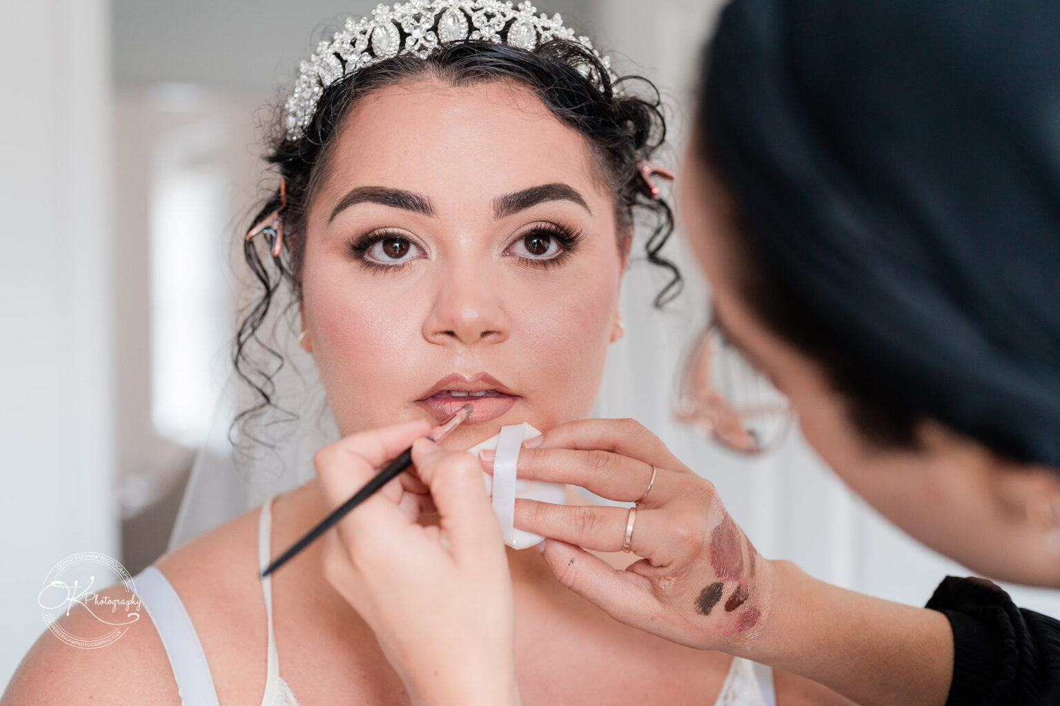 Symphony Rooms Wedding Photography A woman in a tiara having her makeup applied by a makeup artist.