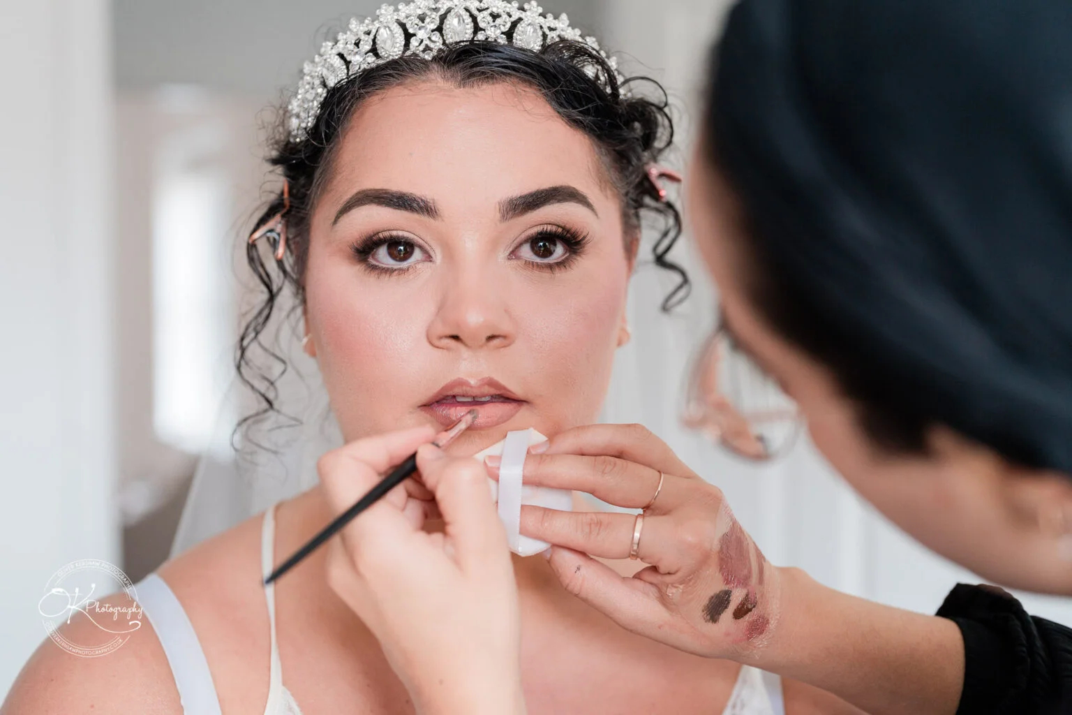 A woman in a tiara having her makeup applied by a makeup artist.