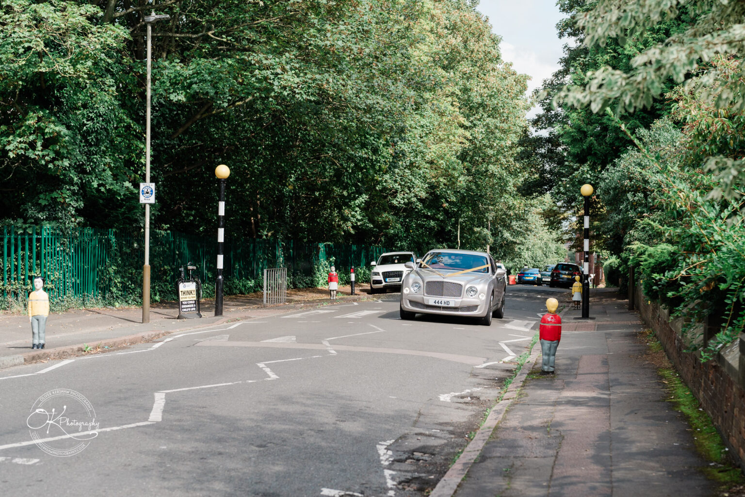 Symphony Rooms Wedding Photography A silver luxury car driving down a tree-lined suburban street, with bollards shaped like toy soldiers on the sidewalk.