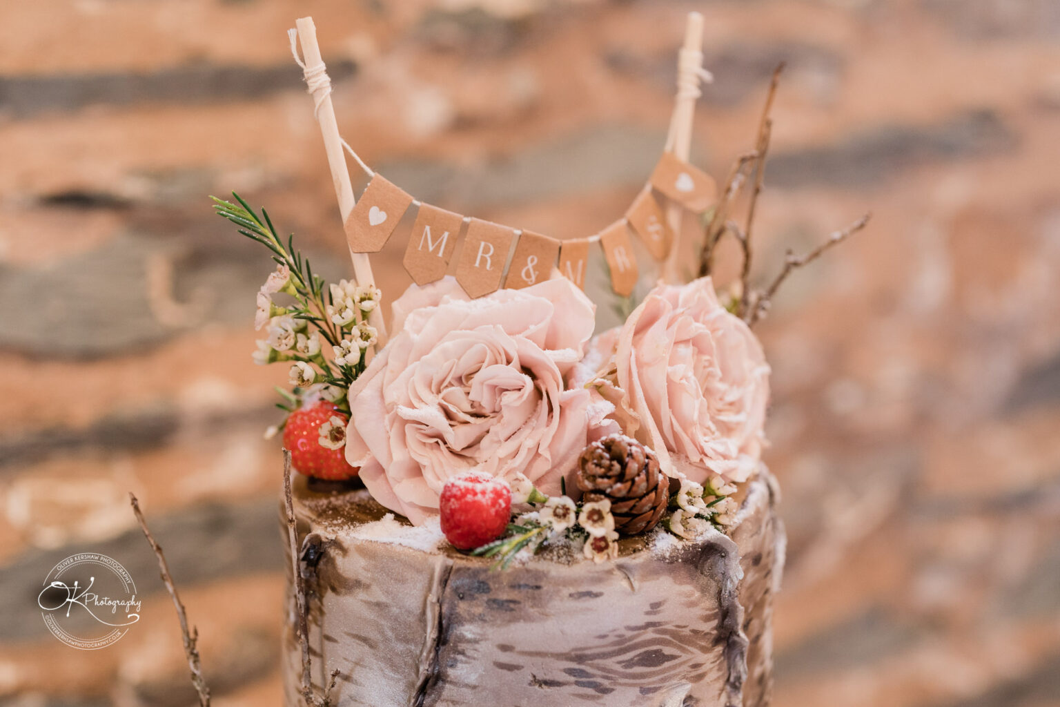 The Old Stables Wedding Photography Wedding cake decorated with pink roses, berries, pinecones, and branches, with a bunting topper that reads "MR & MRS."