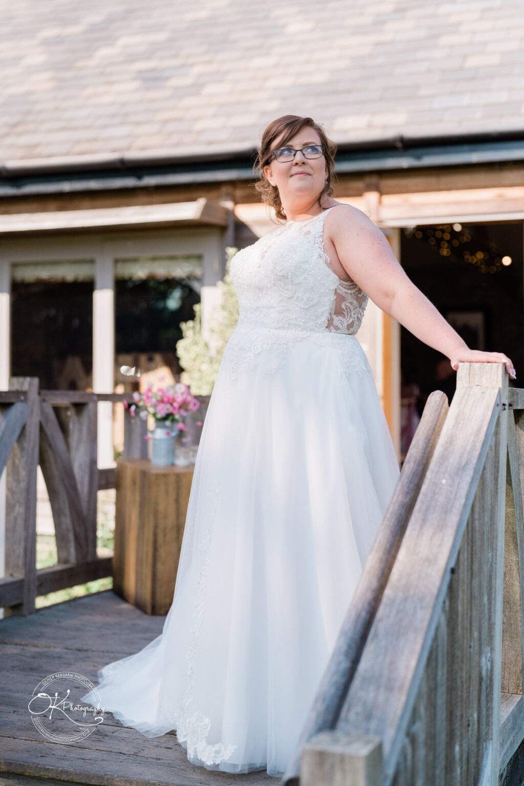 The Old Stables Wedding Photography Bride in white lace wedding dress posing on a wooden bridge in front of a rustic building.