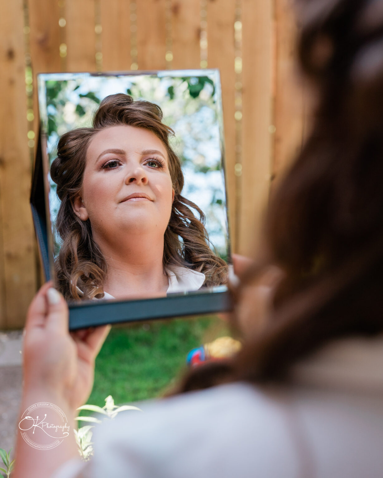 The Old Stables Wedding Photography Woman holding a mirror and looking at her reflection with a wooden fence in the background.