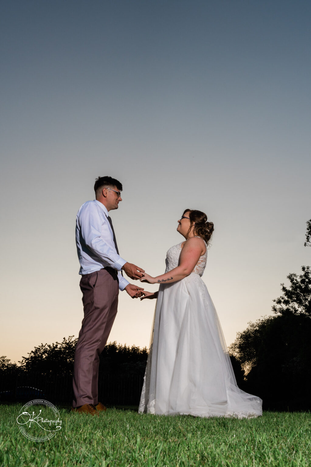 The Old Stables Wedding Photography Bride and groom holding hands and looking at each other on a grassy lawn during sunset.