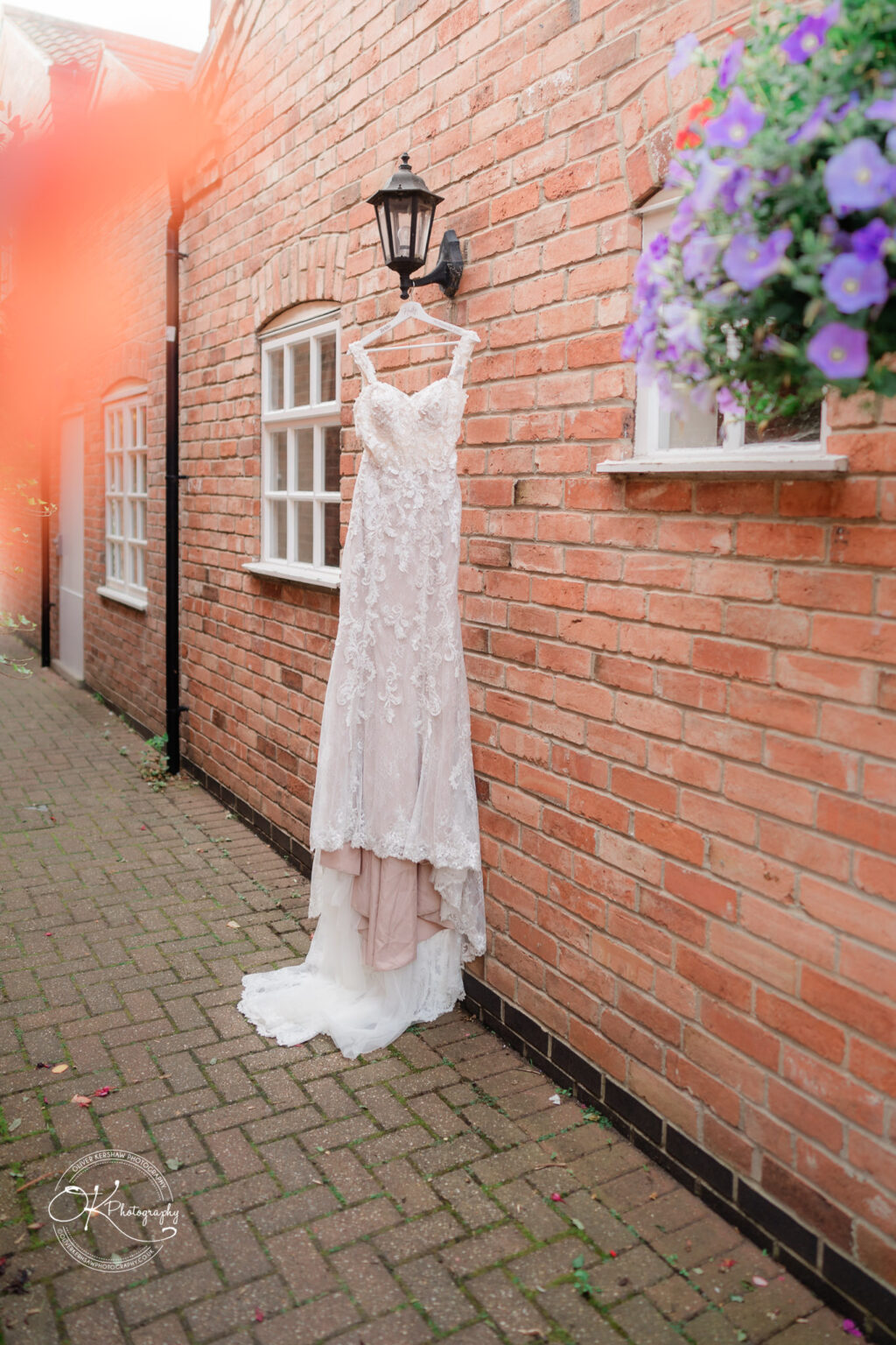 The cottage hotel - Wedding Photography Wedding dress hanging on a wall-mounted lantern outside a brick building.