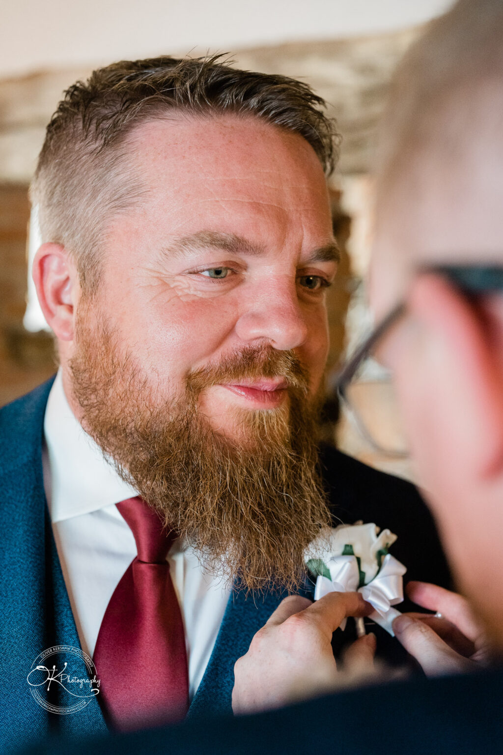 The cottage hotel - Wedding Photography A man wearing a suit and tie smiles as another person adjusts his boutonniere.