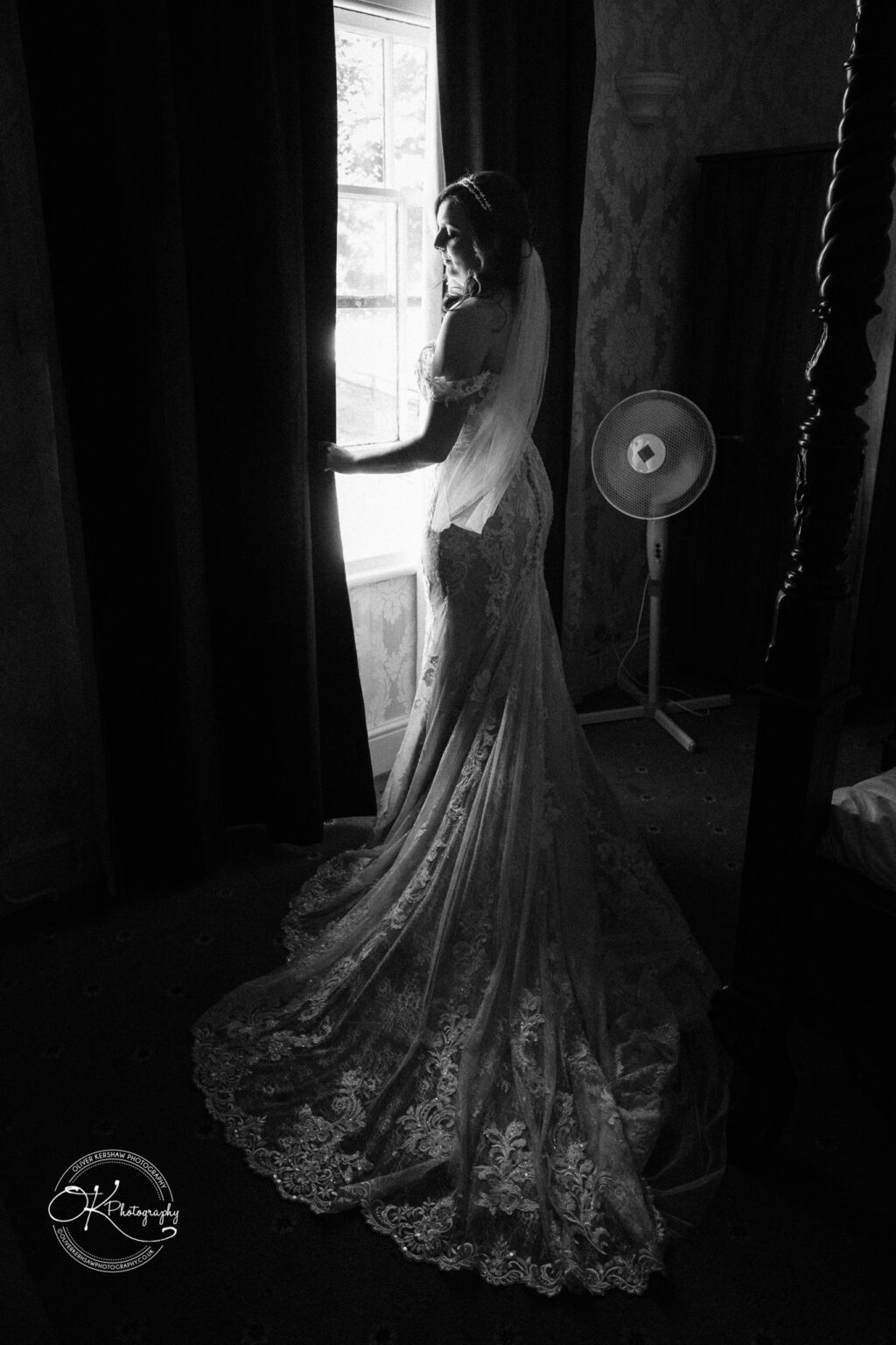 The cottage hotel - Wedding Photography Bride in lace wedding dress looking out window in dimly lit room.