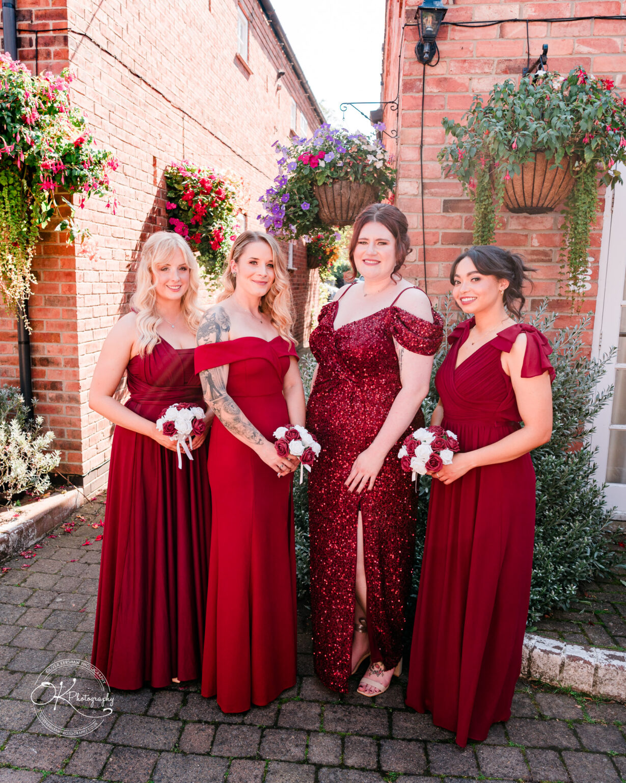 The cottage hotel - Wedding Photography Four women in red dresses posing outside between brick buildings with hanging flower baskets.
