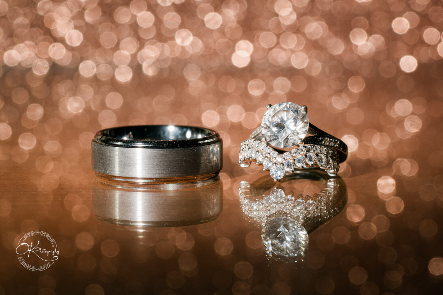 The cottage hotel - Wedding Photography Close-up of a wedding ring set, including a diamond engagement ring and a silver wedding band, against a sparkling bokeh background.
