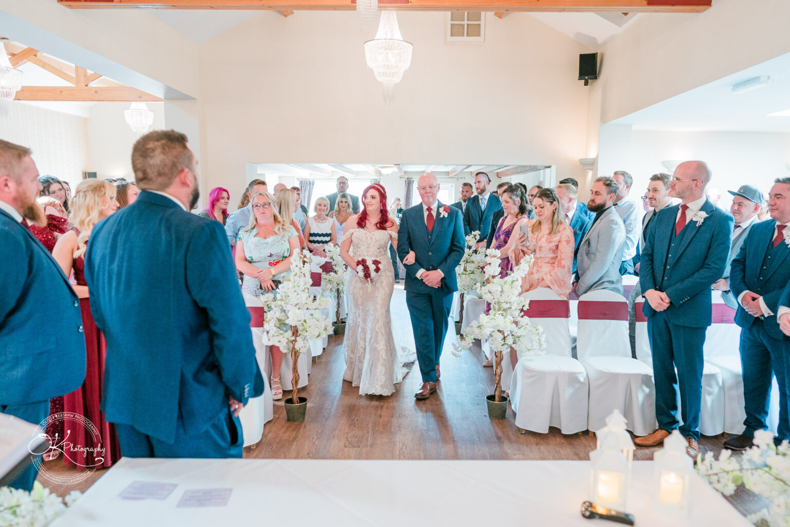 The cottage hotel - Wedding Photography Bride walking down the aisle with her father in a decorated wedding venue, surrounded by guests.