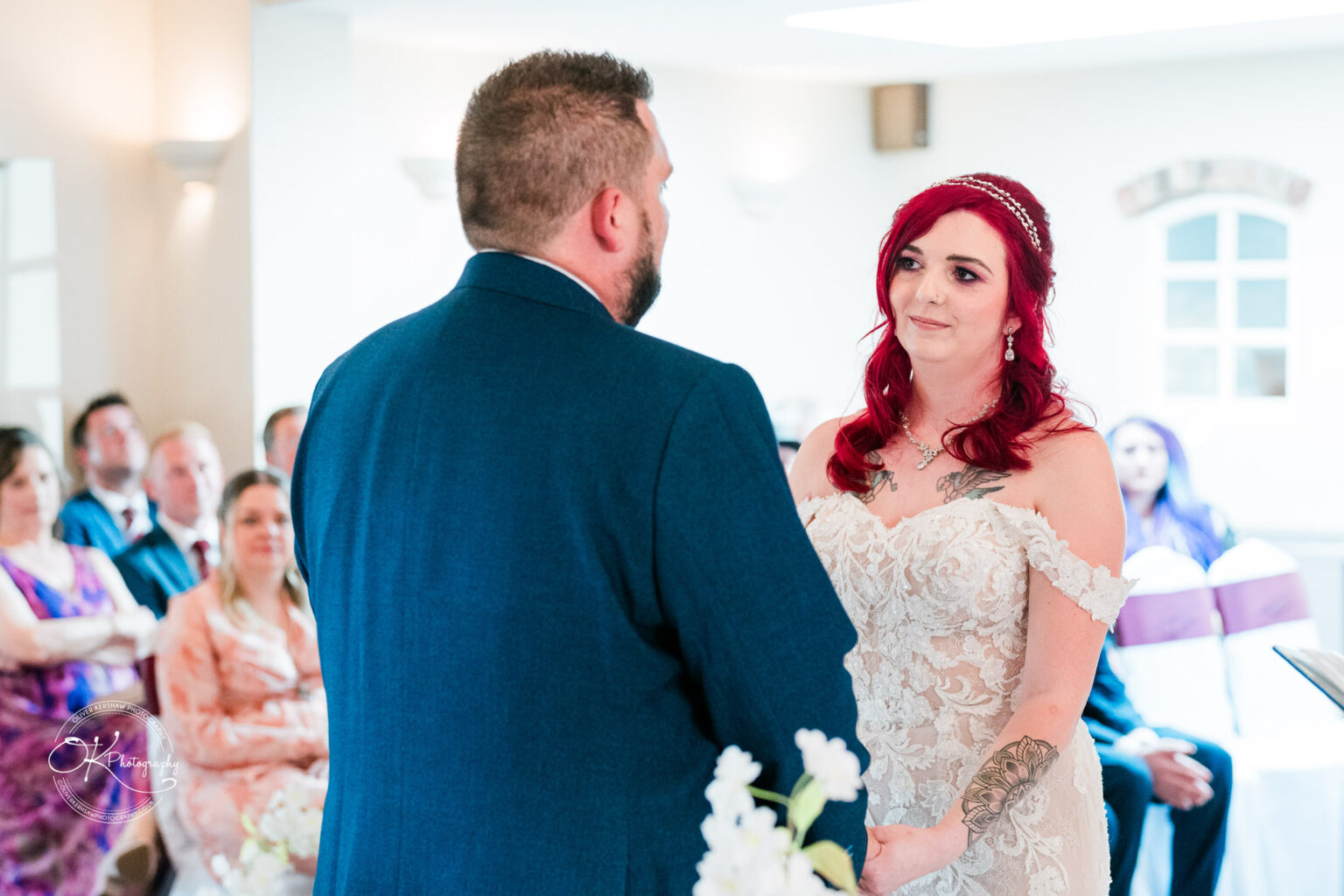 The cottage hotel - Wedding Photography A bride and groom standing and holding hands during a wedding ceremony, with guests seated and watching in the background.