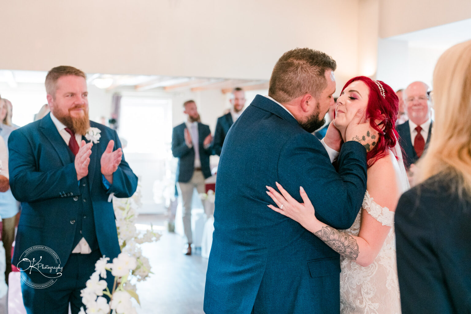 The cottage hotel - Wedding Photography A newlywed couple kissing during their wedding ceremony, surrounded by applauding guests.