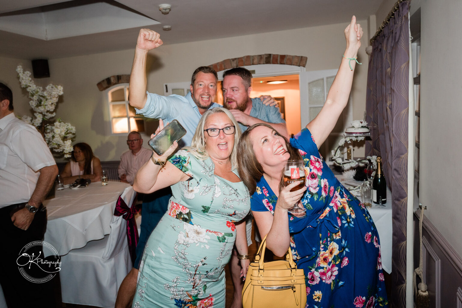 The cottage hotel - Wedding Photography Group of people celebrating and posing enthusiastically inside a room with a table and decorations in the background.