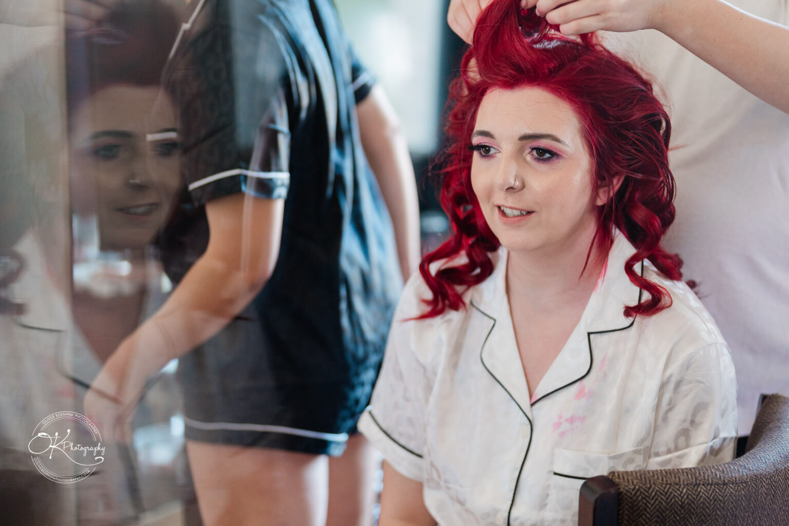 The cottage hotel - Wedding Photography A woman with bright red hair is having her hair styled, wearing white pyjamas, with her reflection visible on the left.