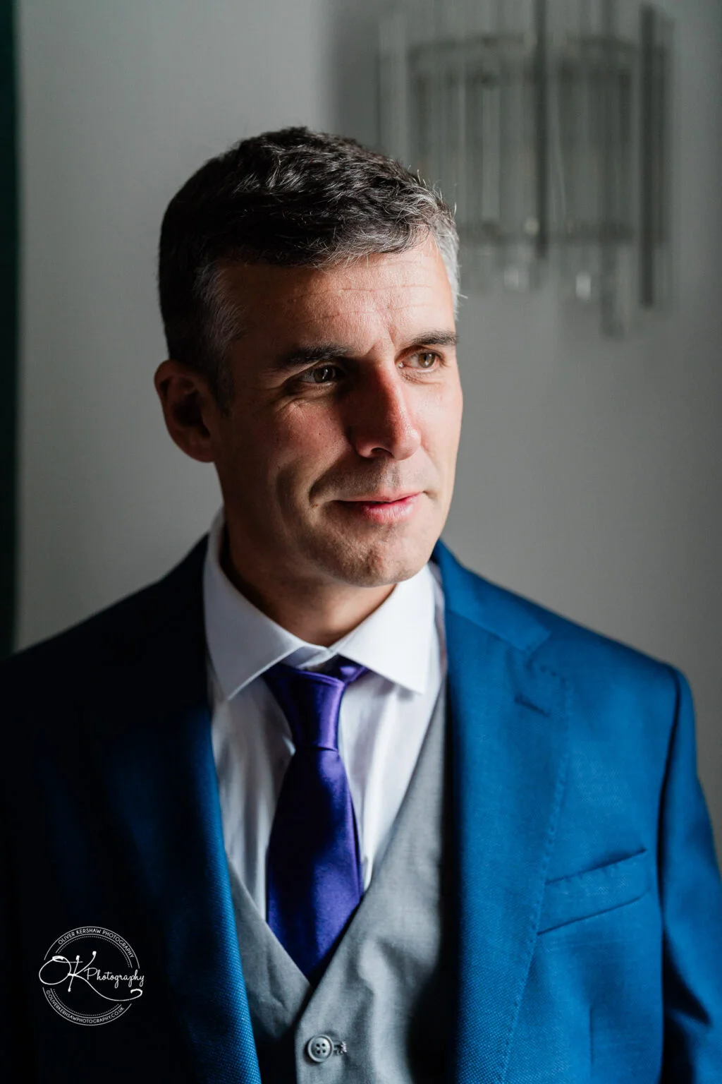 Makeney Hall Hotel - Wedding Photography Man in a blue suit and purple tie, standing in a well-lit room with a neutral background.