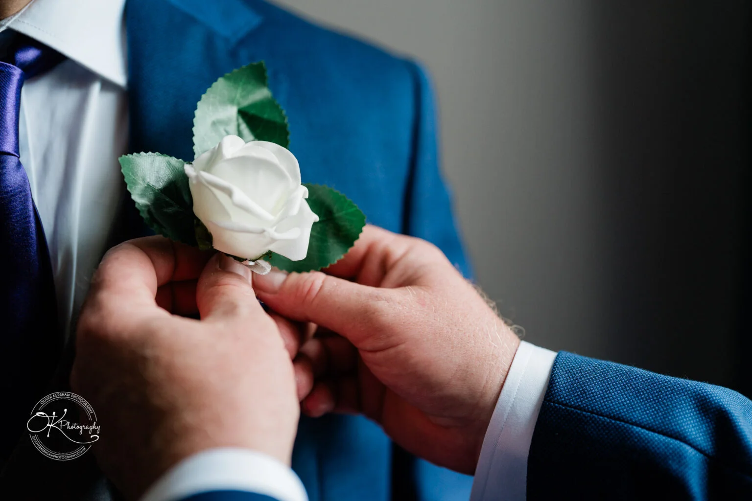 Makeney Hall Hotel - Wedding Photography A person pinning a white rose boutonnière to another person's blue suit.