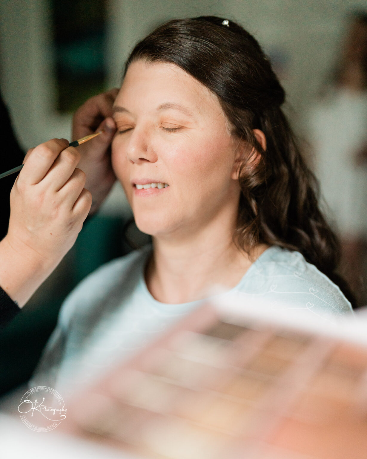 A woman with eyes closed having makeup applied.